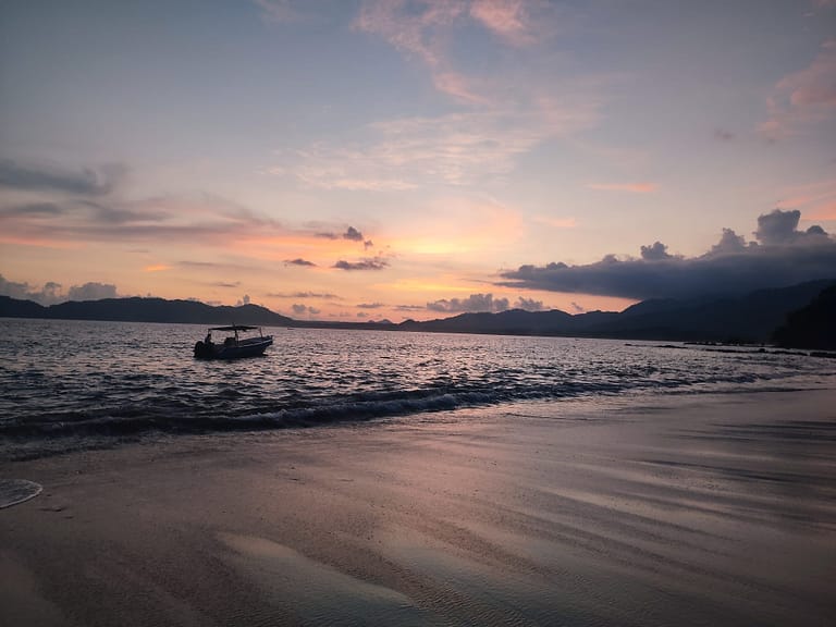 Image of a beach at sunset with a small boat just off the shore